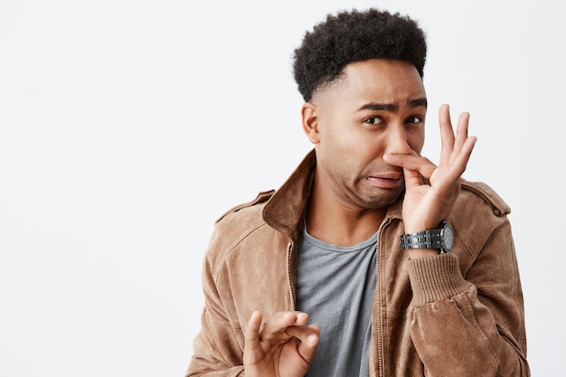 Ha un cattivo odore. chiuda sul ritratto di giovane uomo dalla pelle scura divertente con il naso di chiusura dell'acconciatura afro con le dita, sentendo l'annuncio dall'odore disgustoso dalla discarica della spazzatura in città.