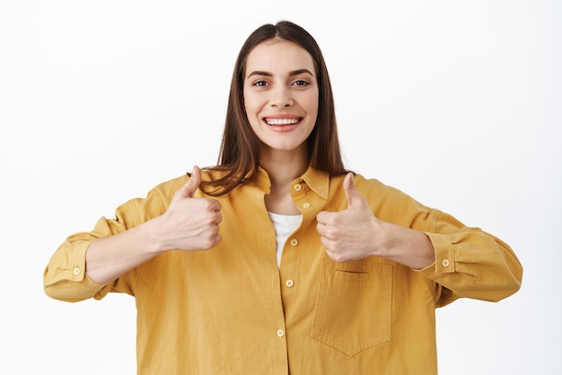 Free photo that was super good smiling caucasian woman shows thumbs up in support like and approve good thing say yes praise great offer recommending company white background