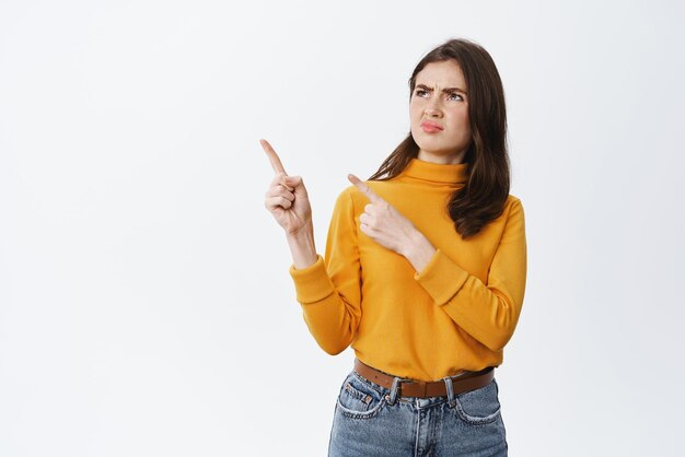 Thats gross Disgusted young woman frowning pointing and looking left at bad disgusting thing dislike and condemn something standing against white background