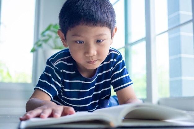 Мальчик собирается читать книги или делать домашнее задание. дети учатся дома во время школьных каникул. образовательные концепции для чтения, онлайн-обучение