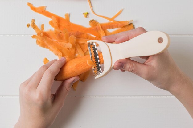 Ребенок тщательно чистит морковь специальным ножом. морковь чистим специальным ножом.