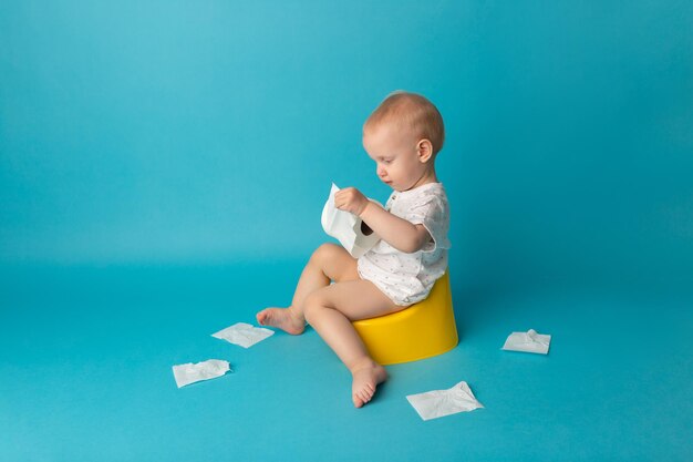 Ребенок сидит на горшке и разворачивает туалетную бумагу на цветном фоне