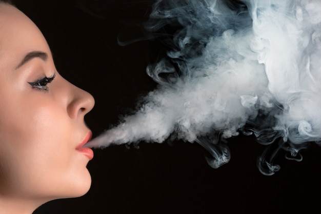 무료 사진 검은 스튜디오에서 vaping 젊은 여자의 얼굴