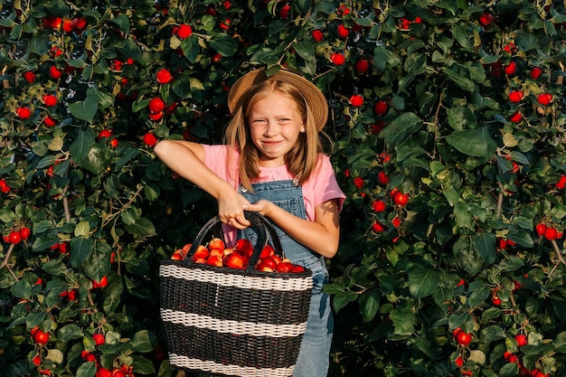 그 소녀는 사과 바구니를 들고 감사의 수확을 배경으로 사과 나무에서 미소를 짓습니다