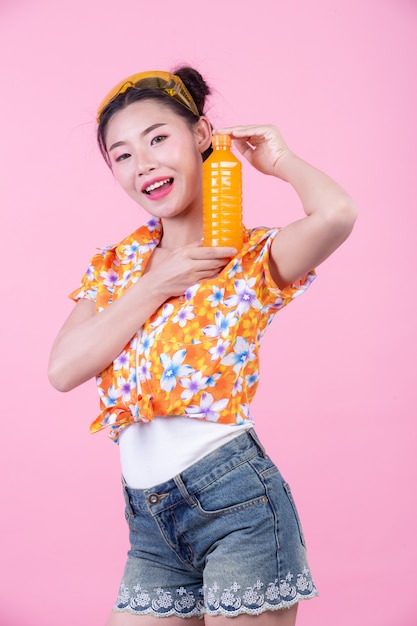 Девушка держит бутылку апельсинового сока на розовом фоне.