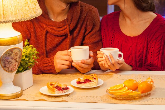 Счастливая молодая пара с чашками чая и пирожными.