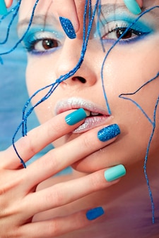 頭に光沢のある飾りが付いた砂の光沢のあるカラフルなネイルデザインの青い化粧とマニキュアの少女のイメージ。