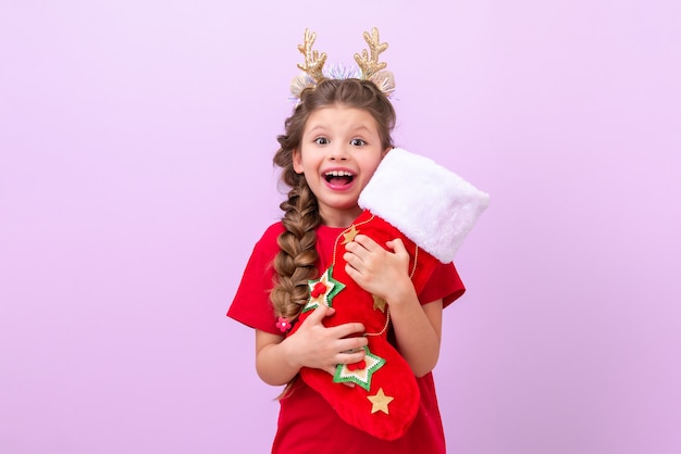 小さな​女の子​は​子供​の​クリスマス​の​角​を​身​に​着けており​、​彼女​は​彼女​の​手​に​贈り物​の​袋​を​持っています​。