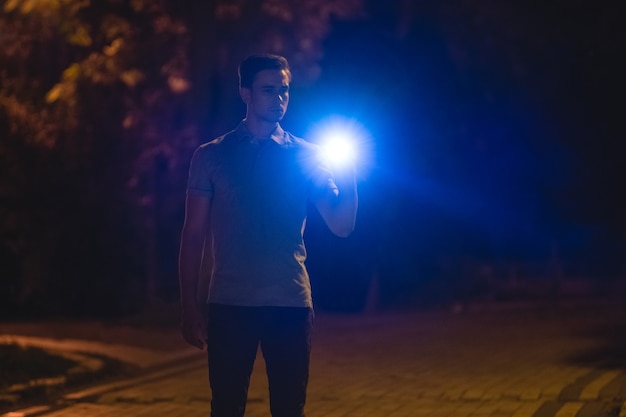 男は暗い路地に懐中電灯を持って立っている。夜の時間