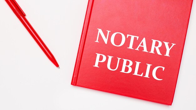 Текст «нотариус публика» написан в красном блокноте рядом с красной ручкой на белом столе в офисе. бизнес-концепция