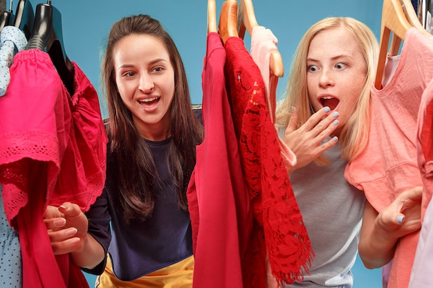 Две молодые красивые девушки смотрят на платья и примеряют их, выбирая в магазине
