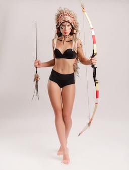 Женщина в образе коренных народов америки с луком и стрелами позирует на белом фоне