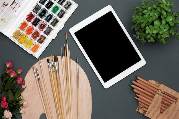 Бесплатное фото Рабочая область художника с ноутбуком, краски, кисти, цветы на черном