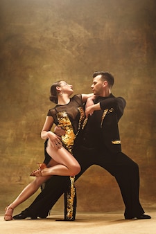 스튜디오 배경에서 관능적 인 포즈로 춤을 추는 금 드레스를 입은 젊은 댄스 볼룸 커플. 탱고를 추는 전문 댄서. 볼룸 댄스 개념입니다. 인간의 감정 - 사랑과 열정