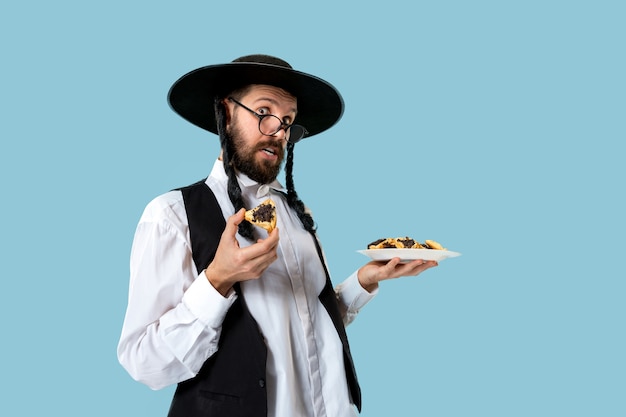 Молодой ортодоксальный еврей в черной шляпе с печеньем hamantaschen на еврейском празднике пурим
