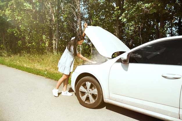 無料写真 若い女性は休憩の途中で車を壊した。彼女は自分で壊れたものを直そうとしている、またはヒッチハイクする必要があります。緊張する