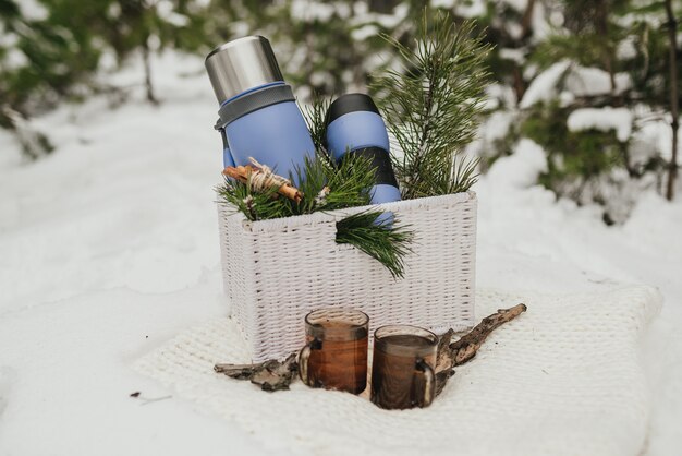 Thermocup, thermos with cup of tea and pine branches lying in a basket 