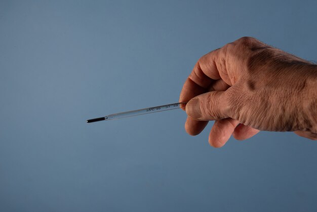 Thermometer in the hands of a doctor isolated on the blue background for Coronavirus prevention