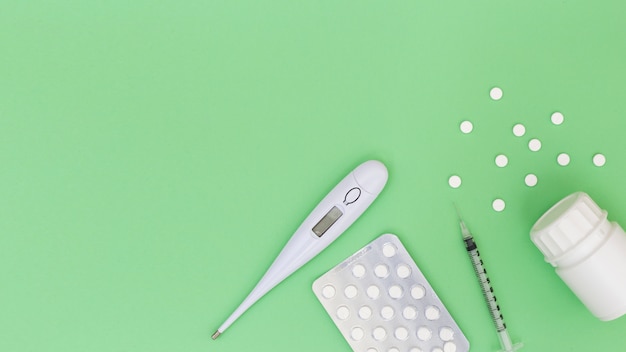Thermometer; pills; syringe and plastic bottle on green background