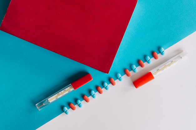 Thermometer; red paper; tablets on dual background