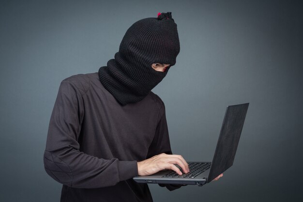 Thieves hold credit cards using a laptop computer for password hacking activities.