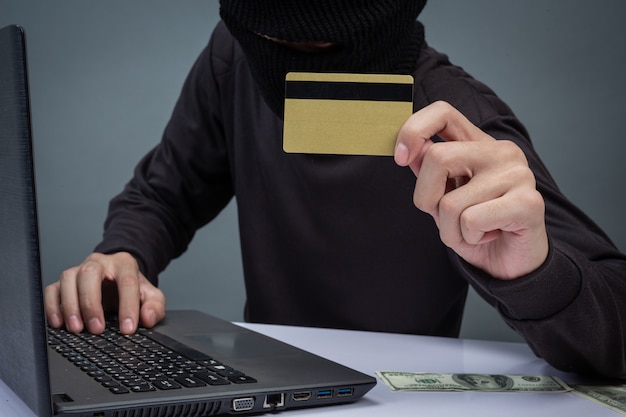 Thieves hold credit cards using a laptop computer for password hacking activities. 