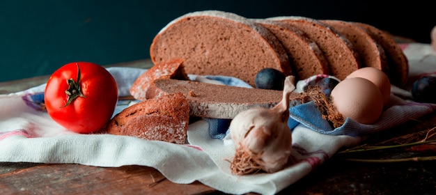 Thin sliced black bread on a white towel with garlic and tomato. 