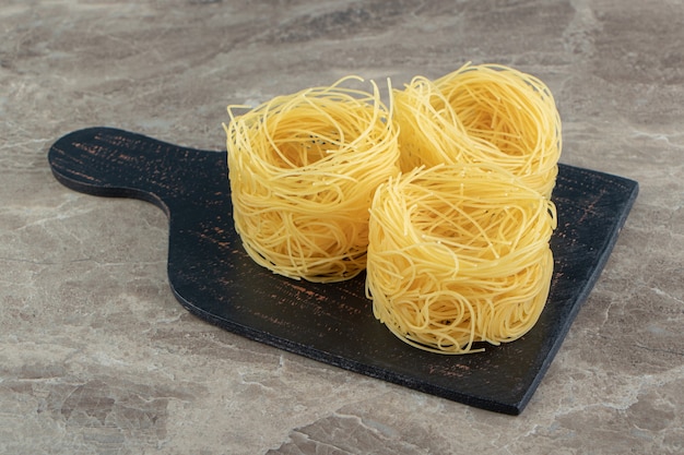 Тонкие спагетти-гнезда на деревянной доске.