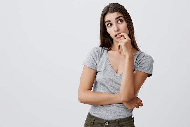 Thinking about presents for Christmas. Portrait of young good-looking sexy caucasian girl with dark long hair in fashionable casual outfit holding hand near lips