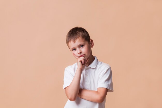 Thinking boy looking at camera standing in front of beige backdrop