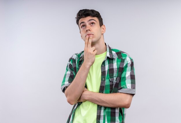 Thinking caucasian young guy wearing green shirt put his fingers on chin on isolated white