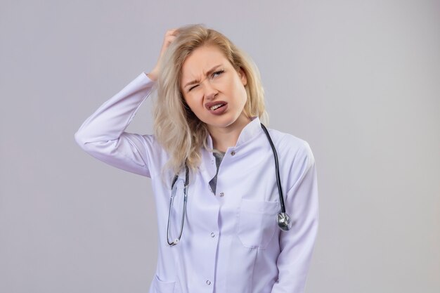 Thinking doctor young girl wearing stethoscope in medical gown grabbed head on white background