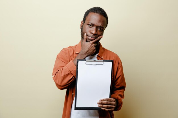 Thinking grabbed chin young african american male holding clipboard isolated on white background