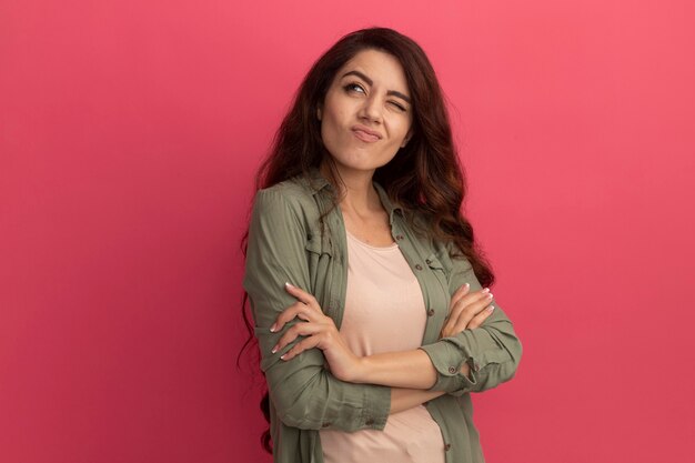 Thinking looking at side young beautiful girl wearing olive green t-shirt crossing hands isolated on pink wall