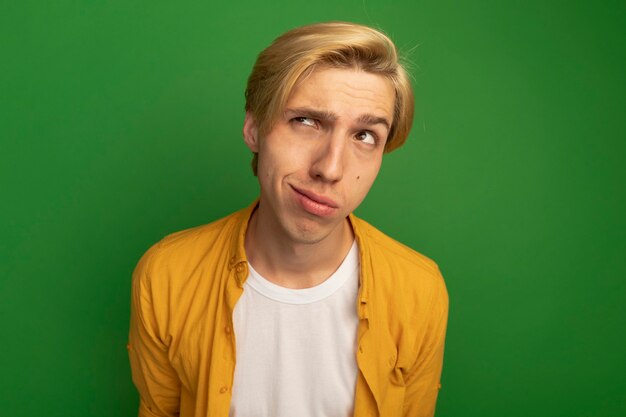 Thinking looking at side young blonde guy wearing yellow t-shirt