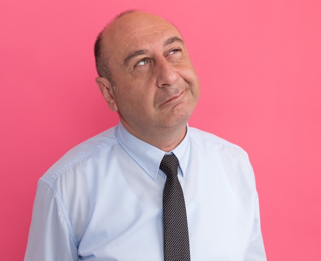 Thinking looking at up middle-aged man wearing white t-shirt with tie isolated on pink wall