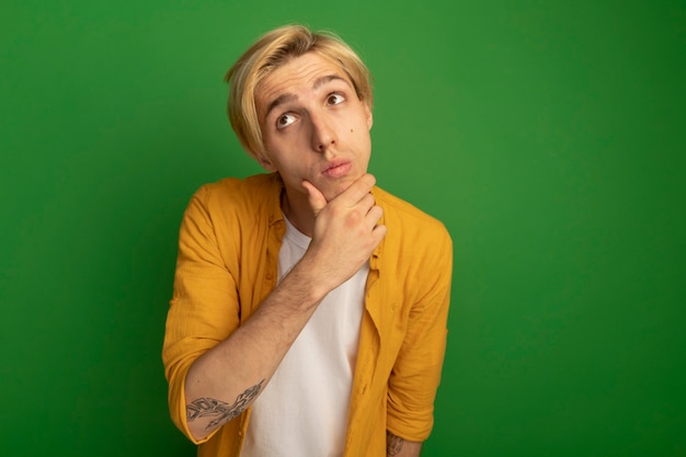 Free photo thinking looking up young blonde guy wearing yellow t-shirt grabbed chin