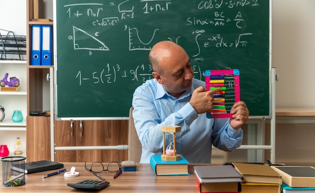 思考中年男性教師は、学用品を持ってテーブルに座って、教室のそろばんを指しています