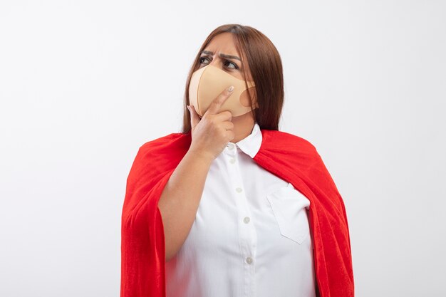 Thinking middle-aged superhero female looking at side wearing medical mask putting hand on chin isolated on white