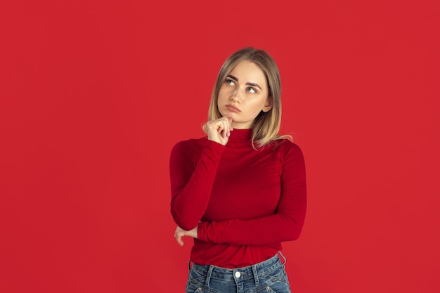 Thinking. Monochrome portrait of young caucasian blonde woman isolated on red studio wall.