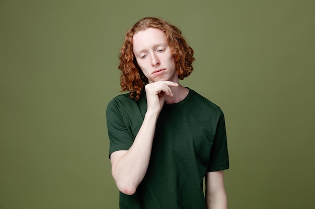 Thinking putting hand on chin young handsome guy wearing green t shirt isolated on green background