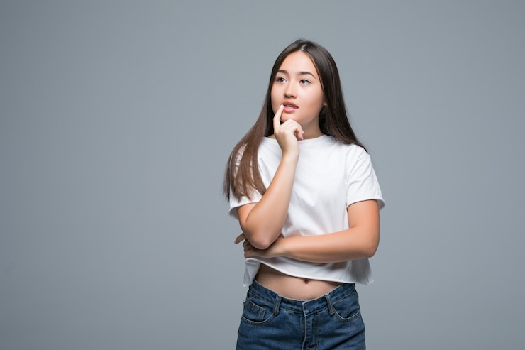 無料Photo よそ見灰色の背景の上に孤立したアジアの若い女性を考えてください。
