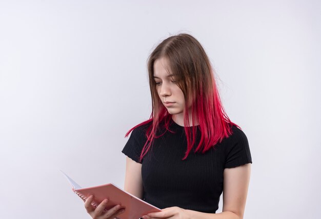 Thinking young beautiful girl wearing black t-shirt looking at notebook on her hand on isolated white wall