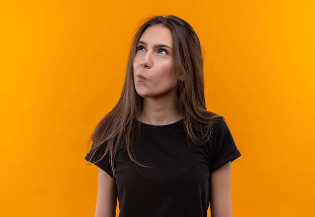 Thinking young caucasian girl wearing black t-shirt looking at side on isolated orange wall