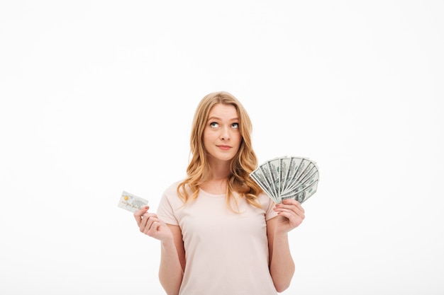 Thinking young lady holding money and credit card.