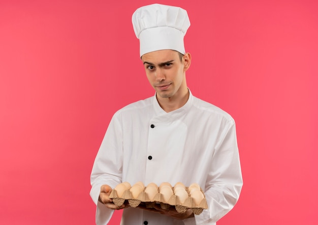 Thinking young male cook wearing chef uniform holding batch of eggs