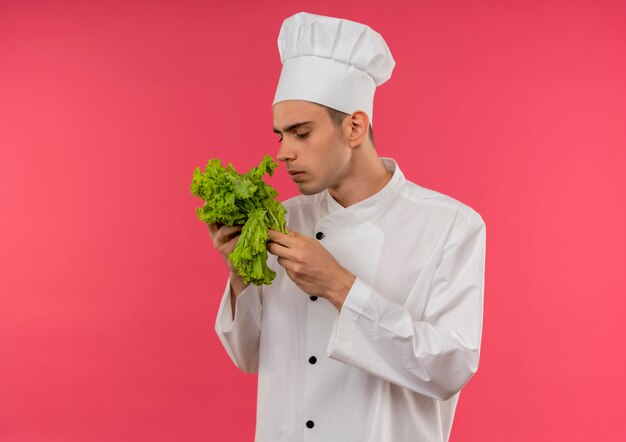 Thinking young male cook wearing chef uniform holding and sniffing salad with copy space
