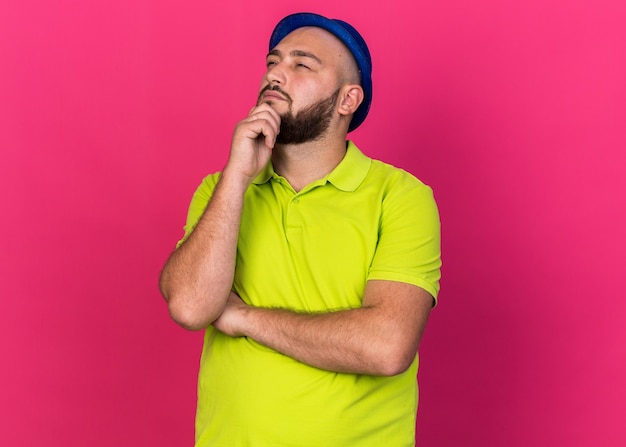 Thinking young man wearing blue party hat grabbed chin 