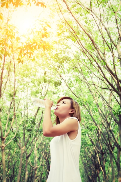 Thirsty girl drinking water with tree branches background