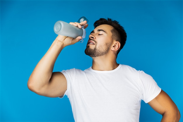 Thirsty handsome guy is drinking from the sport bottle